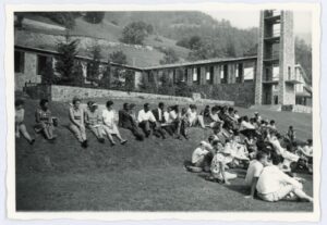 Immagine: Foto in bianco e nero di ragazzi seduti nel prato di Agape. Ghigo e gli edifici che la rappresentano.
