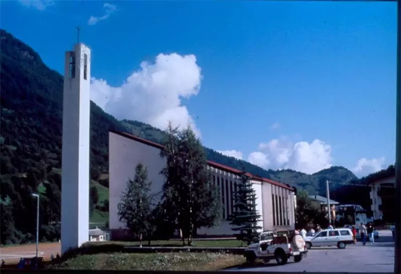 Immagine: Esterno chiesa cattolica di Prali (To). Edificio bianco moderno con campanile anch'esso bianco staccato. Prali egli edifici che la rappresentano II