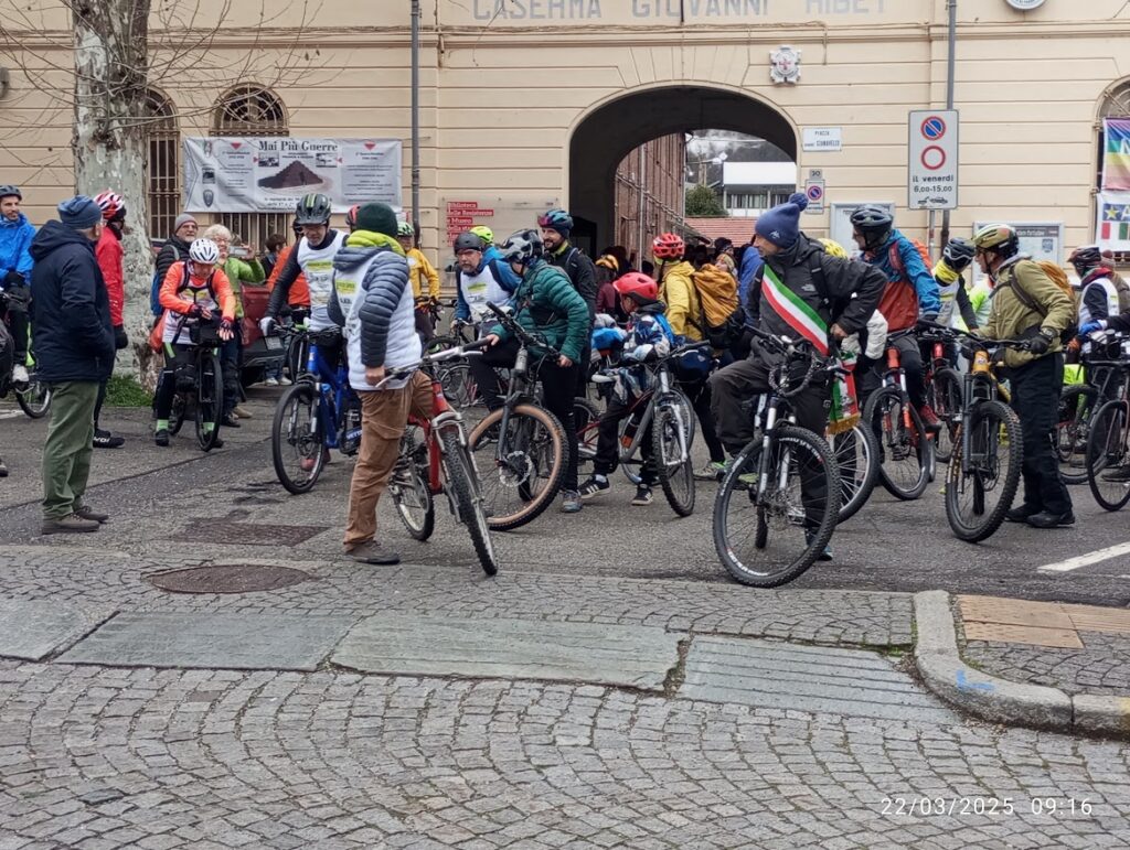 Striscione motivazionale 'Pedalate forte Sognate in grande' e gruppo di ciclisti in partenza, pedalando oltre i limiti, tra comunità e gioia.
