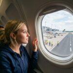 Viaggiare, che passione! Una ragazza bionda osserva sognante la pista dall’oblò, pronta a spiccare il volo verso nuove mete.