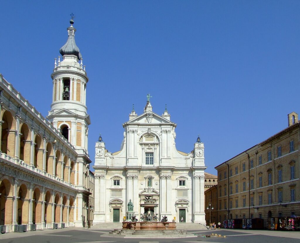 Loreto un luogo antico che parla all'anima: la facciata bianca della Basilica domina la piazza con la fontana e il campanile.