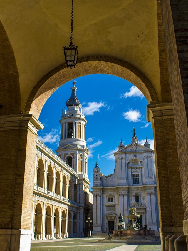 Loreto un luogo antico che parla all'anima: imponente facciata e campanile visti dall'ombra dei portici della piazza.