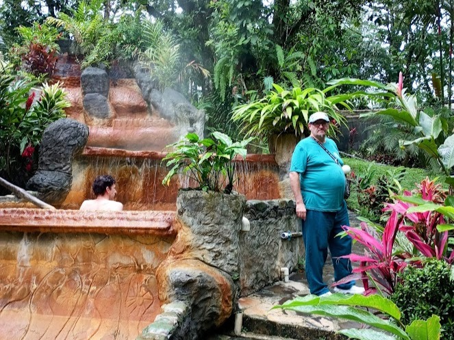 elax e benessere ai piedi del vulcano Arenal per l'uomo in piedi tra piante esotiche, con piscina termale sullo sfondo.