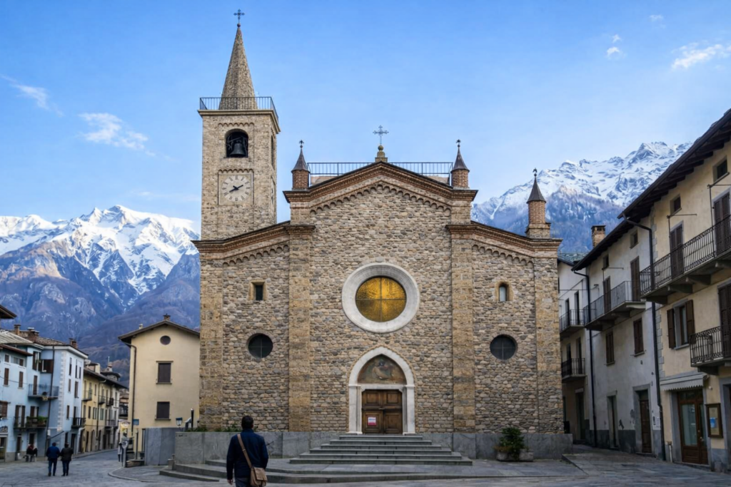 Un gioiello alpino: facciata in pietra della parrocchia di Limone Piemonte con rosone centrale e lunetta affrescata sopra il portale; campanile armonico, sullo sfondo montagne innevate e case del borgo in una piazza silenziosa.