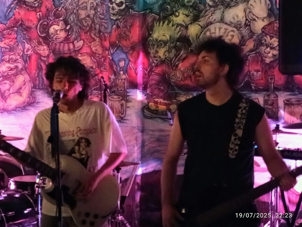 Ale Peiretti e Mane suonano dal vivo chitarra e basso davanti a un murale colorato durante un concerto roc