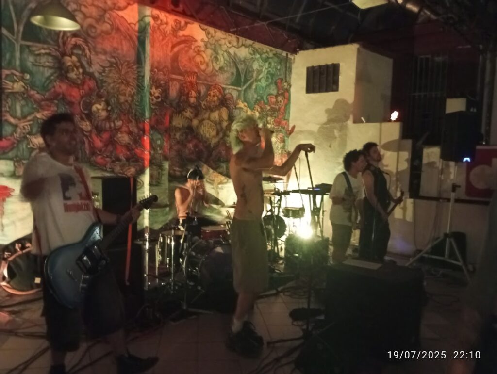 La band al completo con Andrea Ale Peiretti e Mane si esibisce dal vivo sul palco davanti a un grande murale colorato