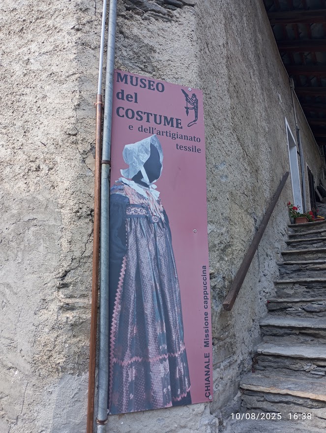 Insegna del Museo del Costume di Chianale (Cn) tra muri in pietra e scalini di ardesia, nel cuore antico e silenzioso del borgo.