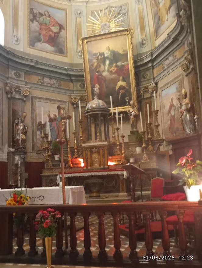 Foto: Interno di chiesa con altare barocco, tabernacolo centrale, dipinti sacri sulle pareti e volta, statue, croce in legno e fiori decorativi
