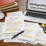 Foto: scrivania con fogli di appunti, caffè, pila di libri e laptop. Abbracciare l'oggi è creare il domani insieme